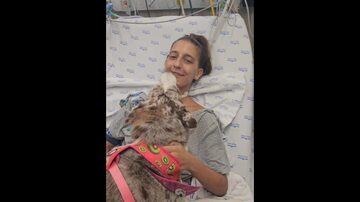 Triatleta Luisa Baptista em uma cama de hospital, com um cão em seu colo. Foto: Reprodução/Instagram @vitorbduarte
