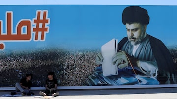 Jovens sentam em frente a outdoor da campanha do clérigo Moqtada al-Sadr, que liderou o bloco vitorioso das eleições no Iraque, em Bagdá. Foto: Thaier Al-Sudani / Reuters
