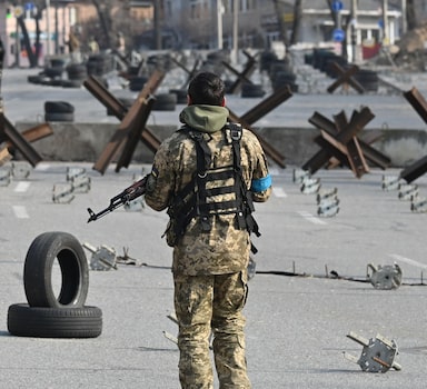 A Ukrainian soldier passes by anti-tank protection elements as he stands guard at a checkpoint in the outskirt of Kyiv on March 28, 2022. (Photo by Sergei SUPINSKY / AFP)