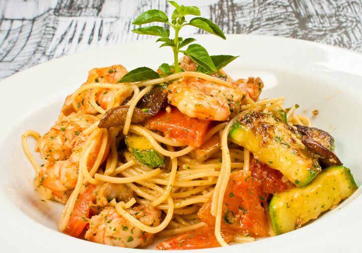 Em um prato fundo de louça branco está o spaguettini com camarão e legumes.