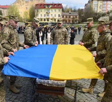 Servicemen drapes the coffin of Ukrainian serviceman who was killed during Russia's invasion of Ukraine, with a Ukrainian flag during his funeral at Lychakiv cemetery in the western Ukrainian city of Lviv on April 28, 2022. (Photo by Yuriy Dyachyshyn / AFP)