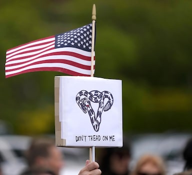 A person holds a sign that reads "Don't Tread On Me" with a uterus-shaped snake and an American  flag, Tuesday, May 3, 2022, during a rally at a park in Seattle in support of abortion rights. (AP Photo/Ted S. Warren)