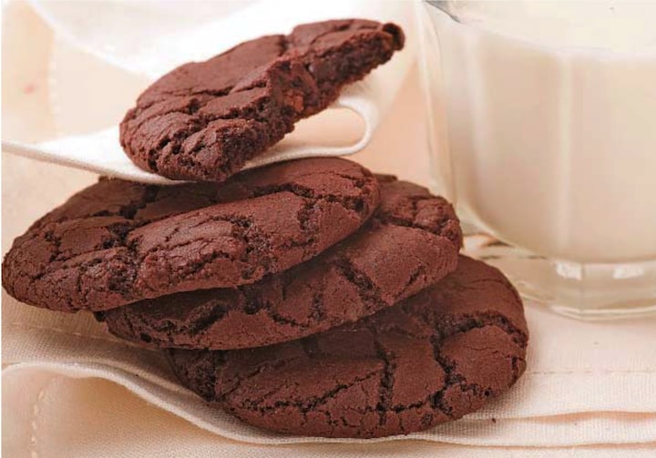 4 cookies de chocolate ao lado de um copo de leite