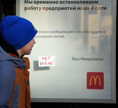 A boy walks past a 'No War!' sign stuck to a window of McDonald's restaurant with a restaurant's closing notice in St. Petersburg, Russia, Tuesday, March 15, 2022. (AP Photo)