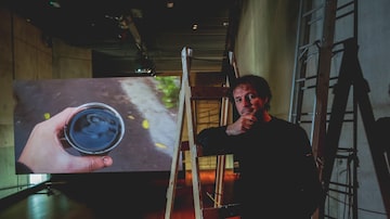 O artista com o vídeo 'Orientações' ao fundo; nele, Bahri percorre ruas filmando um copo com tinta preta em sua mão. Foto: Valéria Gonçalvez/Estadão
