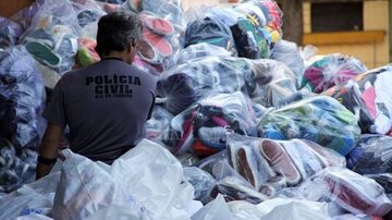 Agente da Polícia Civil em meio a uma pilha de produtos apreendidos durante operação contra pirataria no Rio de Janeiro. . Foto: Marcos Arcoverde/Estadão)