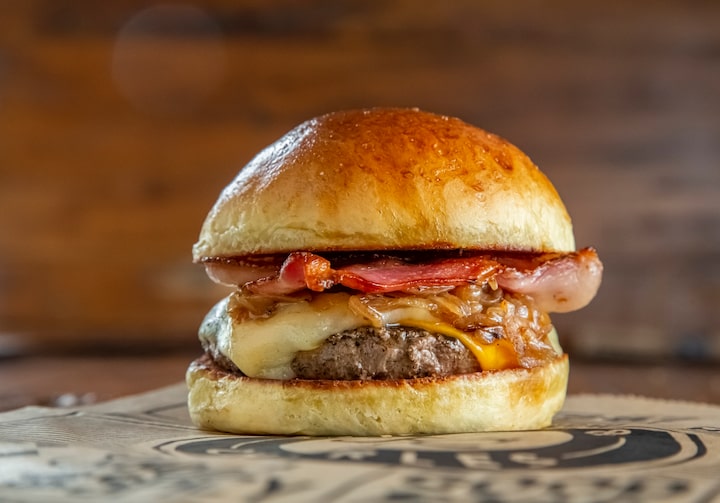 Lanche com hambúrguer, bacon, cebola caramelizada e queijo, sobre superfície com logo da hamburgueria