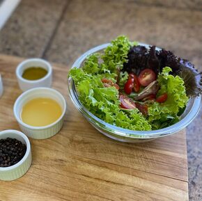 Em uma tábua de madeira, estão potes de ingredientes para molho de salada e, ao lado, uma tigela com alface e tomates cereja picados. Foto: Thaís Barca/Divulgação