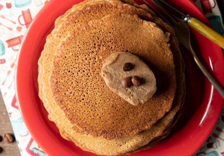 Em um prato de louça vermelho está a panqueca de café com manteiga de café e grãos por cima.
