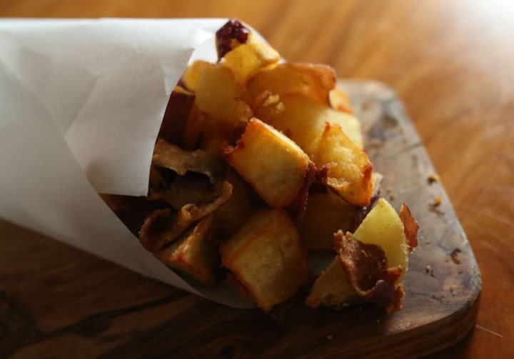 Papel branco enrolado, com batatas-doces fritas, sobre superfície de madeira.