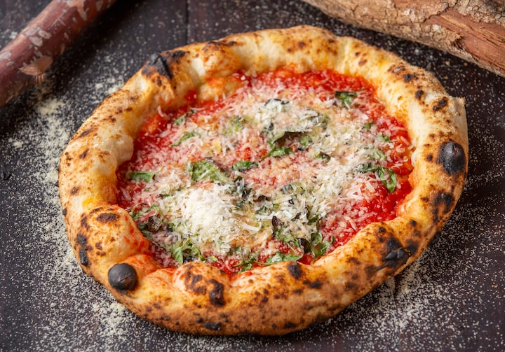 Pizza napolitana com queijo ralado por cima entre duas toras de madeira