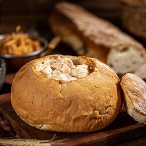 Em um pão italiano redondo, está o camarão aos quatro queijos enfeitado com salsinha por cima. Ao fundo, pão italiano, arroz provençal e batatas rústicas. Foto: Rayane Azevedo/Restaurante Camarões/Divulgação