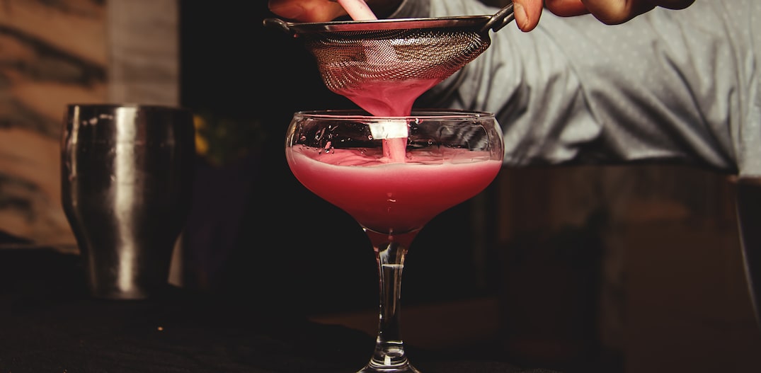 Mãos masculinas preparando drink de líquido vermelho, peneirando. Foto: martina87 | Adobe Stock
