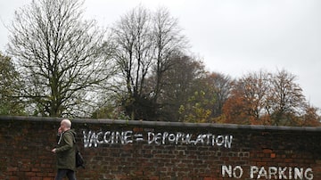 Homem passa por muro com pixação antivacina em Liverpool, na Inglaterra. Foto: Oli SCARFF / AFP