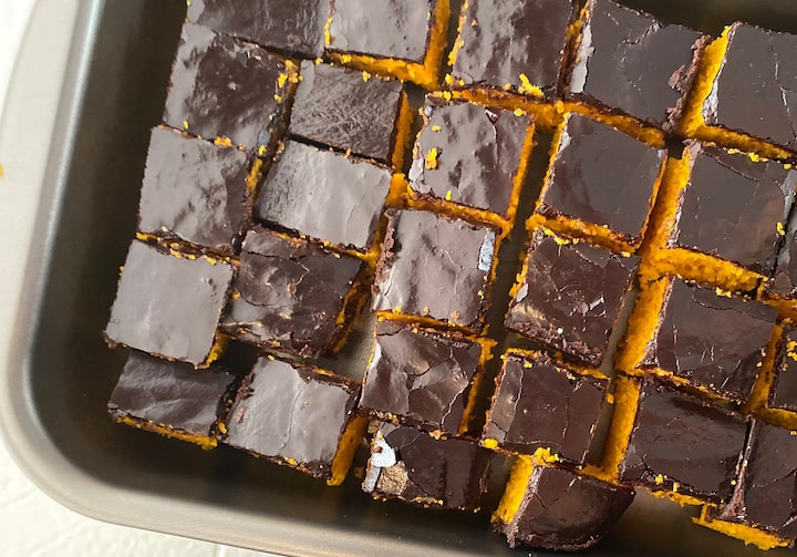 Em uma forma de metal quadrada está um bolo de cenoura com cobertura de chocolate cortado em quadradinhos.