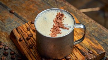 Em uma caneca de metal, está o drink Irish Coffee gelado, com raspas de chocolate enfeitando por cima e grãos de café dispostos na mesa de madeira onde está exposto. Foto: Rodolfo Regini/Divulgação