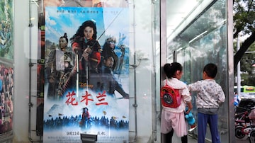 Crianças brincam ao lado de um pôster do filme da Disney 'Mulan'do lado de fora de um cinema em Pequim em 11 de setembro de 2020. Foto: Photo by GREG BAKER / AFP