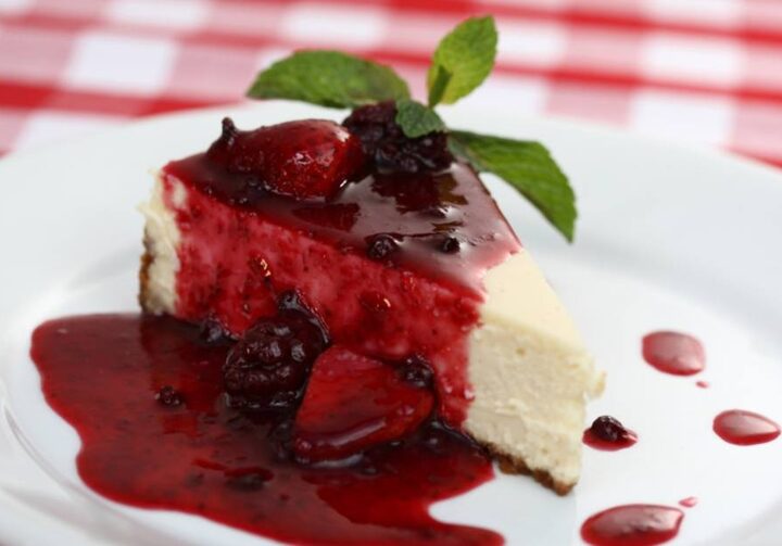Prato branco com cheesecake sobre tecido xadrez vermelho e branco.