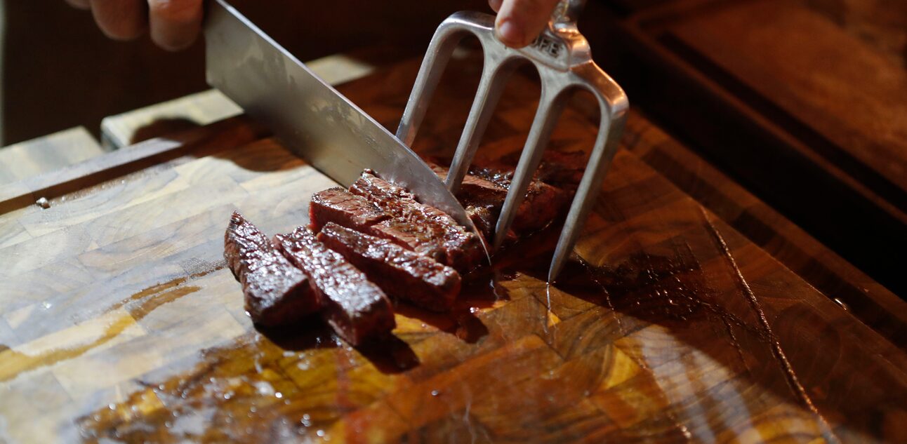 Mãos masculinas cortando carne com garfo de churrasco e faca grande. Foto: ALEX SILVA/ESTADAO