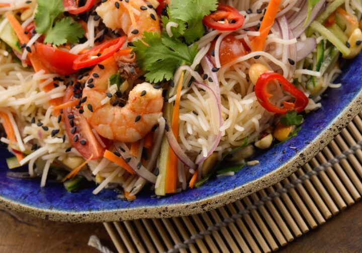 Prato azul com a salada de macarrão de arroz com camarão e hashis ao lado