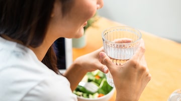 Young female drinking water in glass for refreshing for diet and wellness on table. Beautiful woman happily drink fresh water before breakfast in kitchen in the morning. Healthy food concept. Foto: Chanakon/Adobe Stock