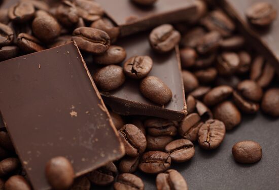 Barra de chocolate em pedaços com vários grãos de café ao lado. Foto: Stepan Popov | Adobe Stock