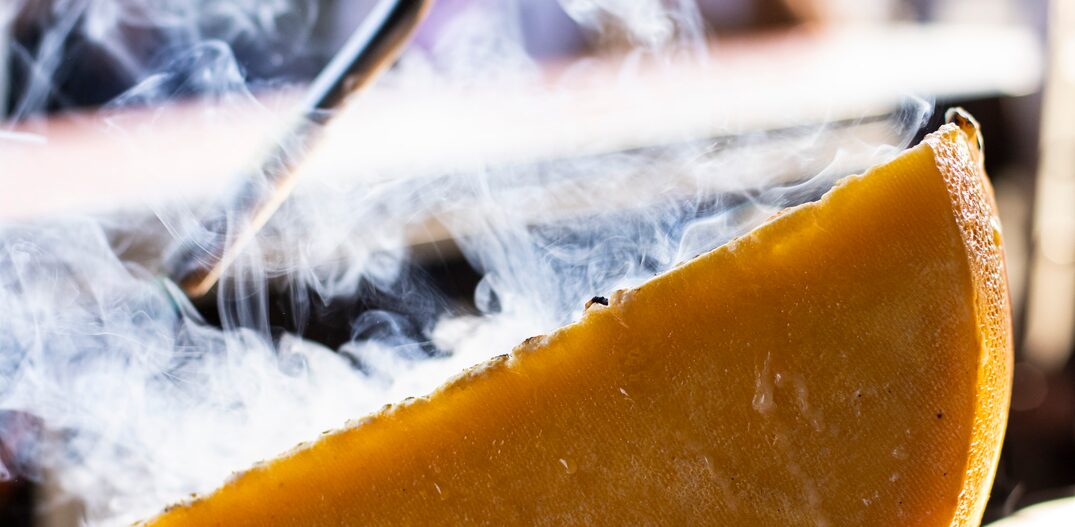 Mão segurando ferramenta de esquentar enquanto outra segura o queijo que sai fumaça. Foto: Marcos Credie | Smorgasburg
