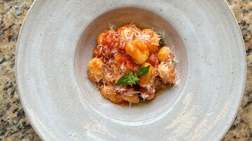 Nhoque de batata com molho ao sugo, servido em prato de porcelana bege, com queijo parmesão ralado e folhas de manjericão, sobre mesa de granito. Foto: Luigi Di Fiore