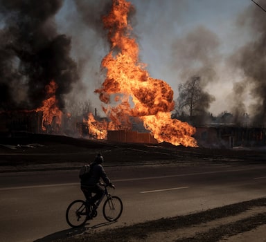 FILE - A man rides his bike past flames and smoke rising from a fire following a Russian attack in Kharkiv, Ukraine, on March 25, 2022. With its aspirations for a quick victory dashed by a stiff Ukrainian resistance, Russia has increasingly focused on grinding down Ukraineâ€™s military in the east in the hope of forcing Kyiv into surrendering part of the countryâ€™s eastern territory to end the war. If Russia succeeds in encircling and destroying the Ukrainian forces in Donbas, the countryâ€™s industrial heartland, it could try to dictate its terms to Kyiv -- and possibly attempt to split the country in two. (AP Photo/Felipe Dana)