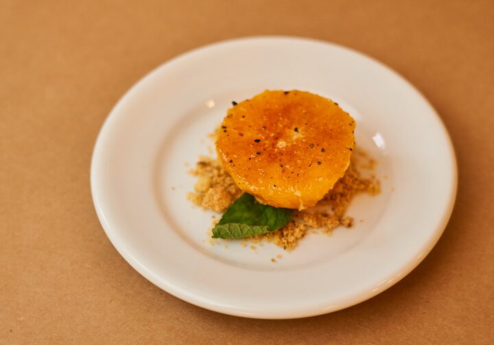 Doce de laranja servido em um prato de sobremesa branco, apoiado em uma mesa na cor laranja.