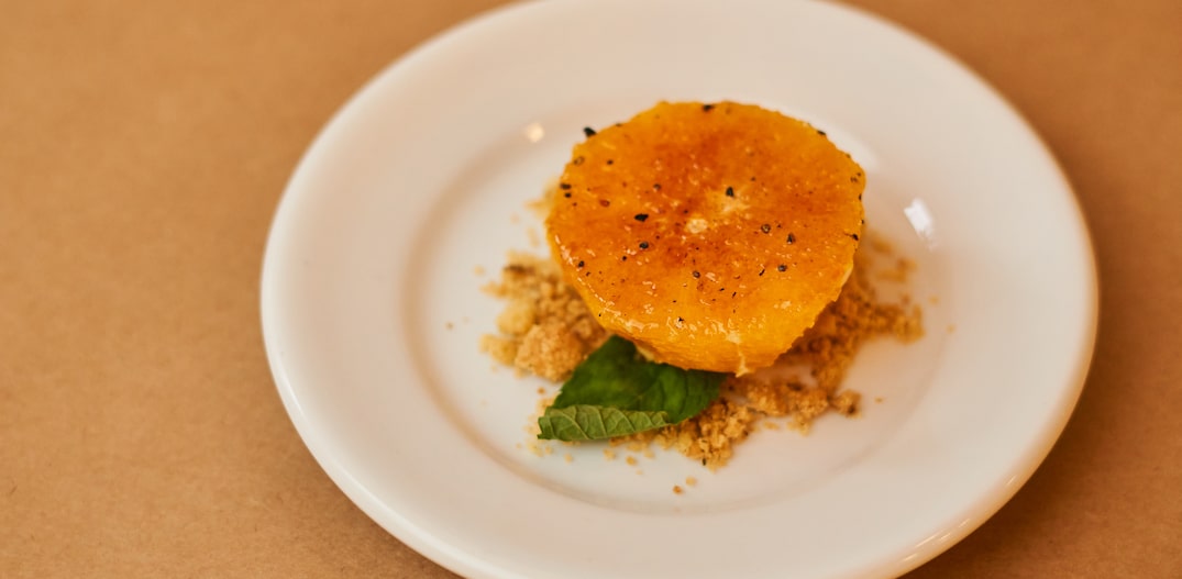 Doce de laranja servido em um prato de sobremesa branco, apoiado em uma mesa na cor laranja. Foto: Laís Acsa