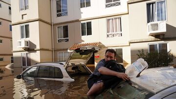 Homem se segura em carro, na cidade de Canoas (RS), enquanto tenta retornar ao seu prédio, que foi alagado pelas chuvas. Foto: Carlos Macedo/AP