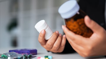 Woman hold bottle of drug tablet painkiller or vitamin supplement reading label ready to organizing medicine at home. medication healthcare concept. Foto: Natee Meepian/Adobe Stock
