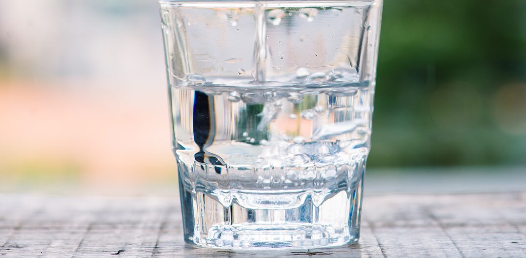 Água em uma garrafa de vidro transparente é despejada em um copo baixo transparente. Foto: makistock/Adobe Stock
