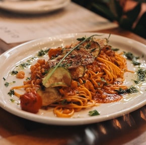 Tagliolini com camarão e chips de abobrinha em um prato sobre mesa de madeira. Foto: Giro Ristobar/Divulgação