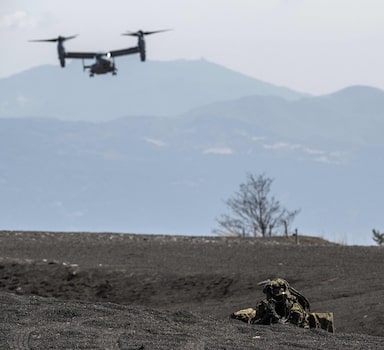 A member of the Japanese Self-Defense Force Amphibious Rapid Deployment Brigade holds position while US Marine Corps MV-22 Osprey tilt-rotor aircraft land during a joint exercise between the two services at the Higashifuji training area in Gotemba, Shizuoka Prefecture on March 15, 2022. (Photo by Charly TRIBALLEAU / AFP)