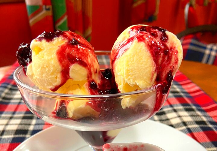 Sobre um prato branco, uma taça com sorvete de creme com calda de frutas vermelhas e pimenta.