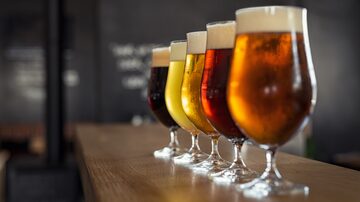 Sobre balcão de madeira e em foco, 5 taças de cerveja de diferentes tipos e cores dispostas enfileiradas. Foto: Rido/Adobe Stock