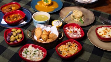 Pratos diversos postos em cima de uma toalha de mesa quadriculada verde. Entre eles, porções de azeitona, frituras e caldos. Foto: Elias Gomes/Divulgação