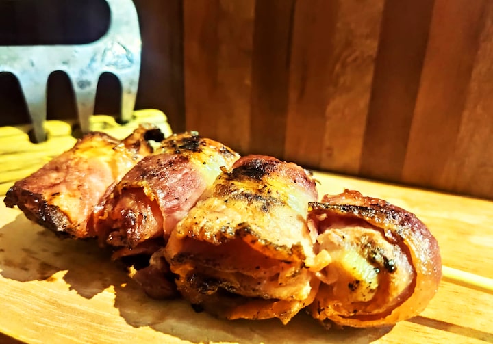 Sobre uma tábua de madeira, medalhões de frango enrolados por fatias de bacon.