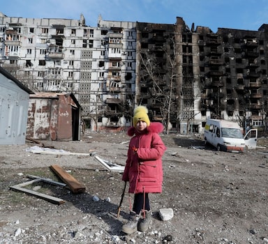 Menina diante de blocos de apartamentos destruídos por bombardeios russos em Mariupol