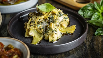 Em foco, uma porção da alcachofra marinada, servida com molho de ervas , alho, e raspas de limão siciliano sobre um prato de cerâmica preta de bordas altas. Foto: Elvis Fernandes