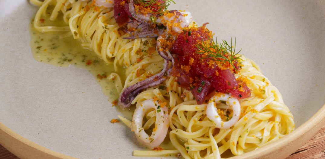 Prato bege de fundo branco servido com espaguete com polvo, camarão rosa, molho rosa e tempero verde. Foto: Plickes | Elea Forneria