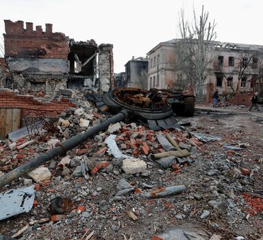 People walk near a destroyed tank and damaged buildings in the course of Ukraine-Russia conflict in the southern port city of Mariupol, Ukraine April 22, 2022. REUTERS/Alexander Ermochenko
