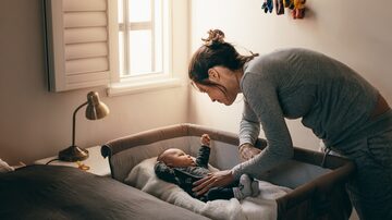 Mother putting her baby to sleep on a bedside baby crib. Woman bending forward over a crib to check her sleeping baby. Foto: Jacob Lund/Adobe Stock