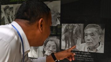 Homem olha foto do ex-chefe da prisão de Tuol Sleng, Kaing Guek Eav. Foto: TANG CHHIN Sothy / AFP