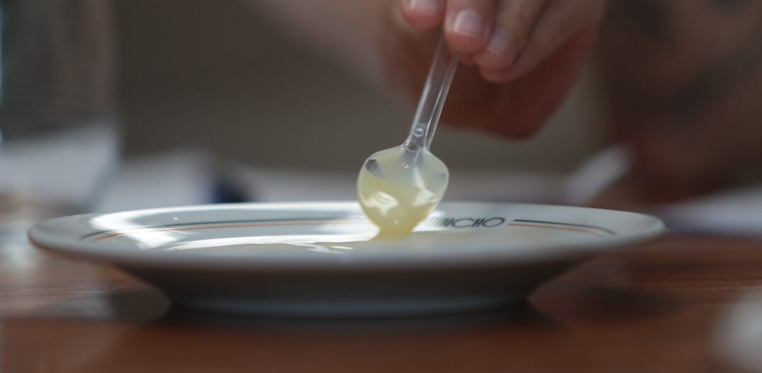 Mão segurando colher de plástico que mexe leite condensado dentro do prato. Foto: Felipe Rau | Estadão