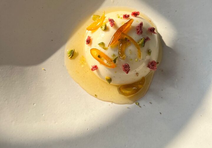 Prato redondo mostra panna cotta decorada com flores, lascas e azeite de laranja Kinkan