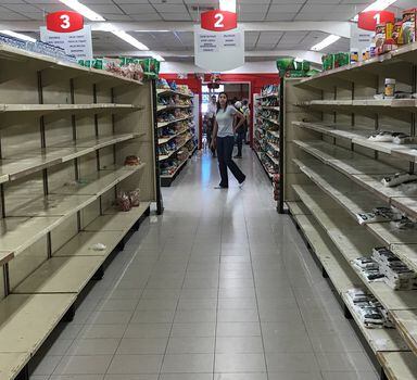 Venezuelana procura por produtos em meio à prateleiras vazias em supermercado de Caracas; situação não melhorou com plano econômico.
